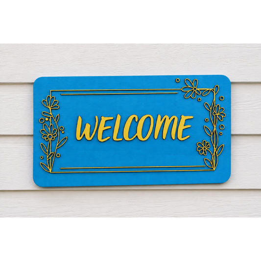 Detail van een houten welkomstbord met het woord WELCOME in verhoogde letters en een decoratieve bloemenrand.